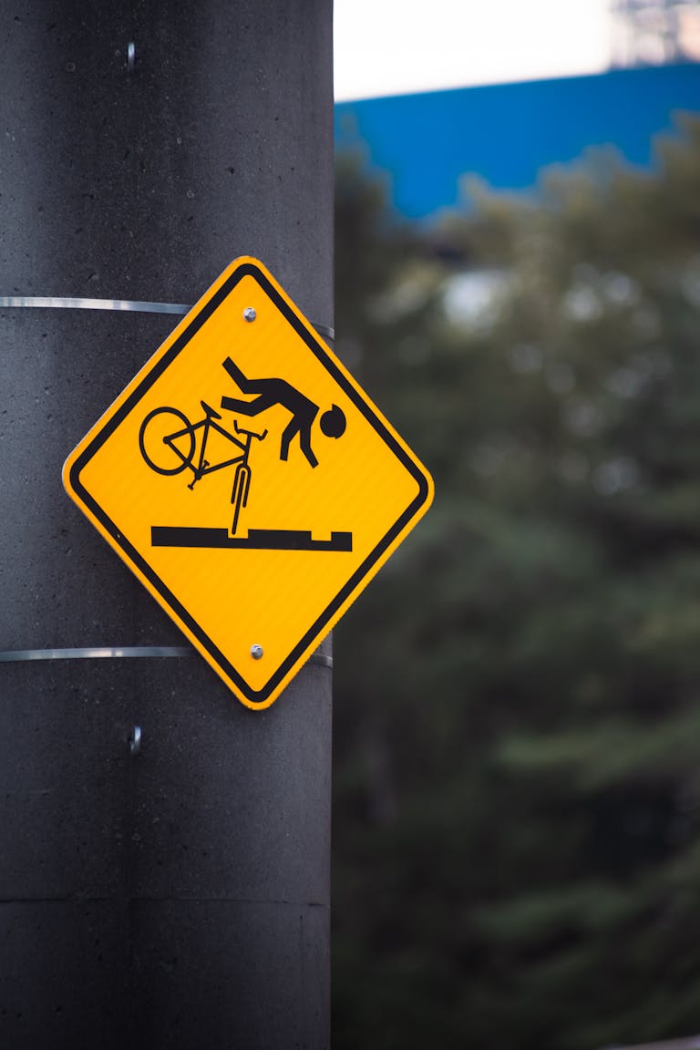A cautionary yellow sign warning cyclists of potential road hazards on a pole.