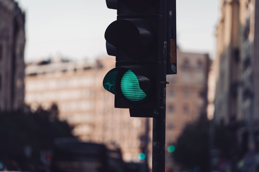 Green traffic light in an urban setting with blurred buildings in the background, conveying movement.