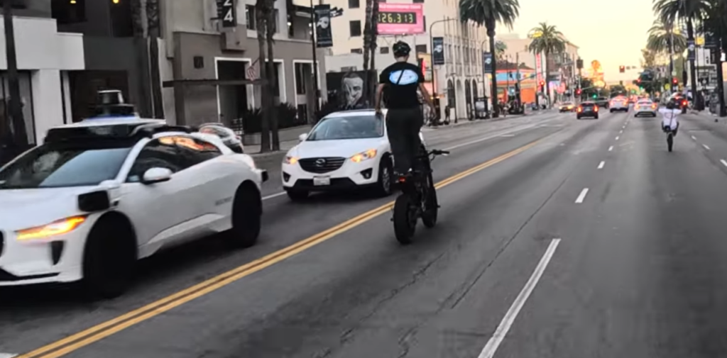 Young rider stands on his bike's seat while gliding past two approaching cars.